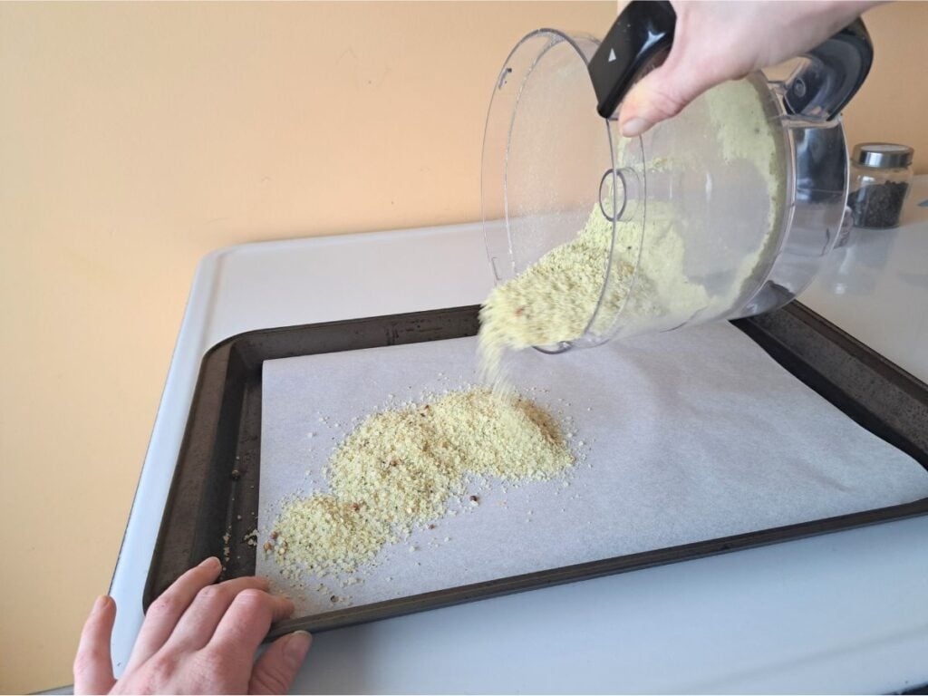 Pouring herb flavored sea salt out on to a parchment lined baking sheet.